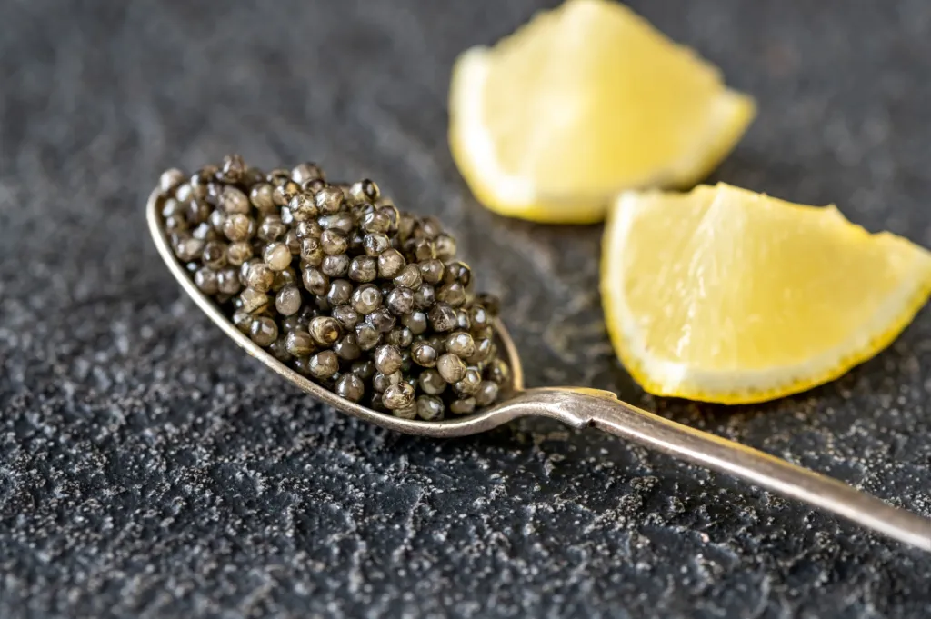 Spoon of black caviar with lemon wedges